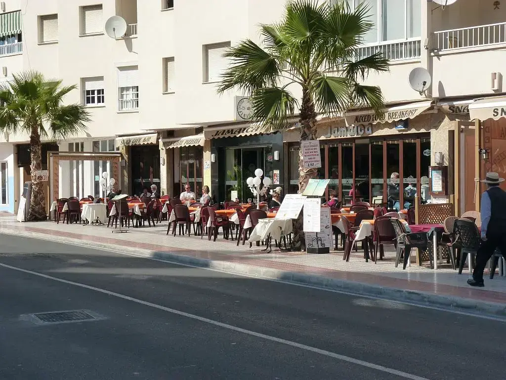 Fachada y terraza del restaurante junto a la calle, con palmeras y pizarras de menú