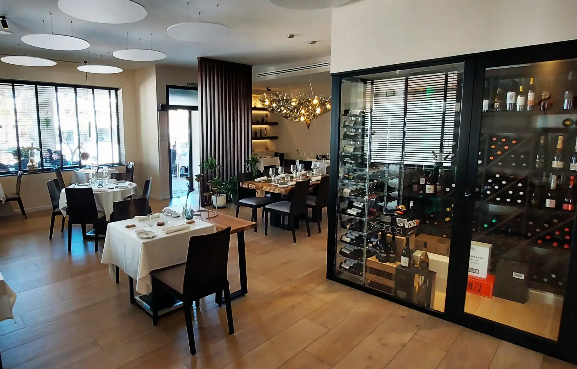 Sala del restaurante con mesas puestas y una gran vitrina acristalada de vinos