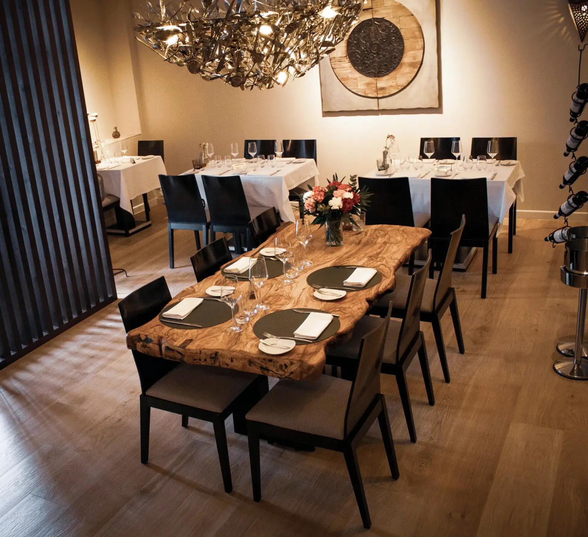 Comedor con mesa de madera de olivo, flores y una gran lámpara metálica