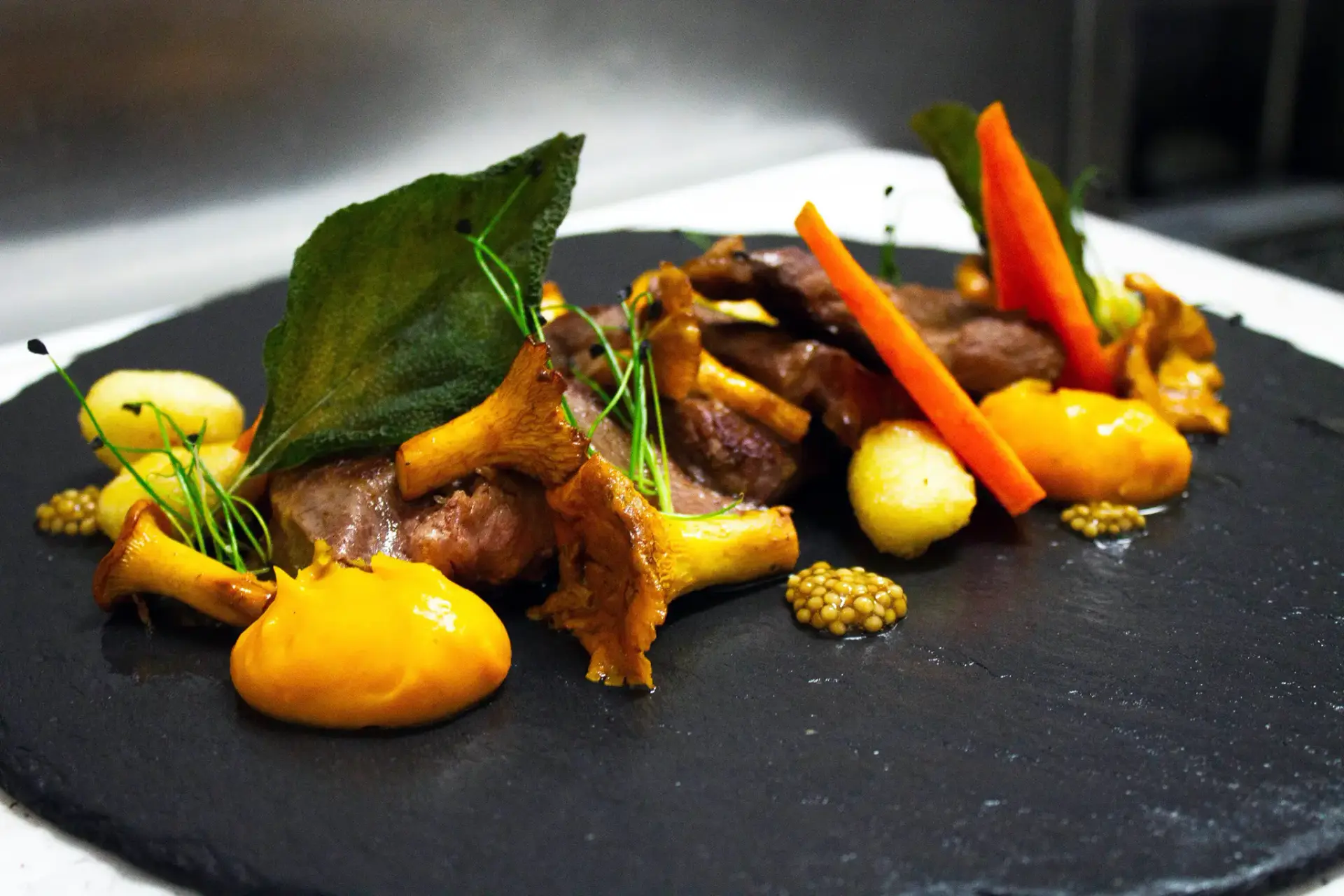 Carne con rebozuelos, puré naranja, zanahoria y mostaza en grano sobre pizarra
