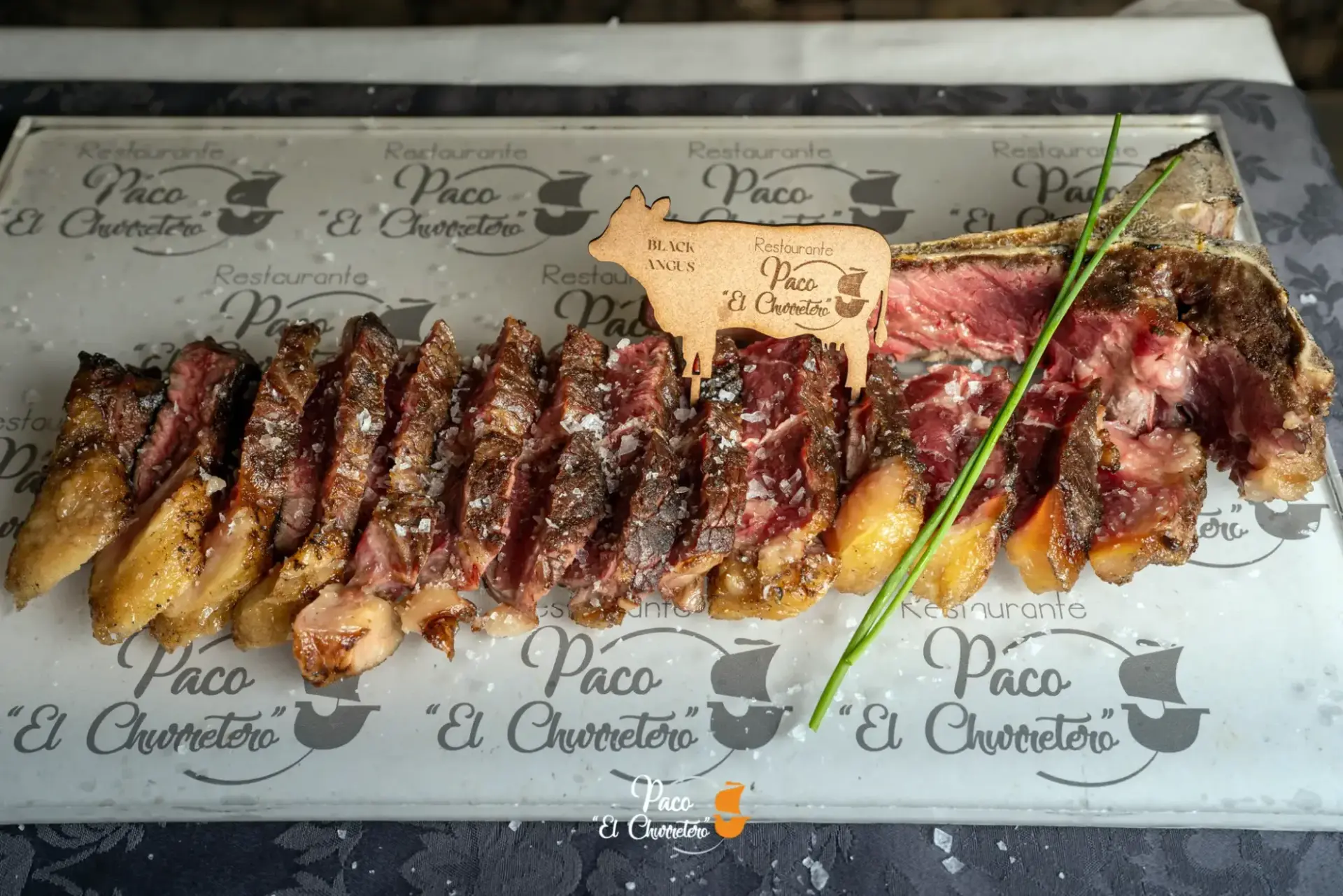 Chuletón de vaca trinchado con patatas asadas sobre bandeja con el logotipo del restaurante