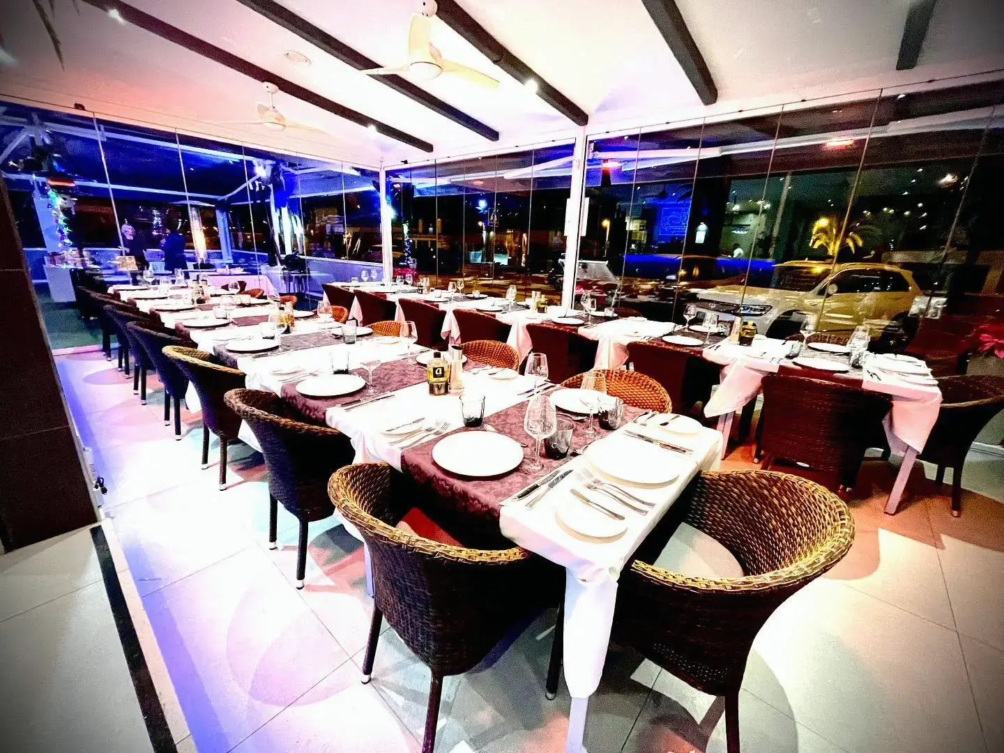 Comedor acristalado con mesas largas montadas y sillas de mimbre por la noche