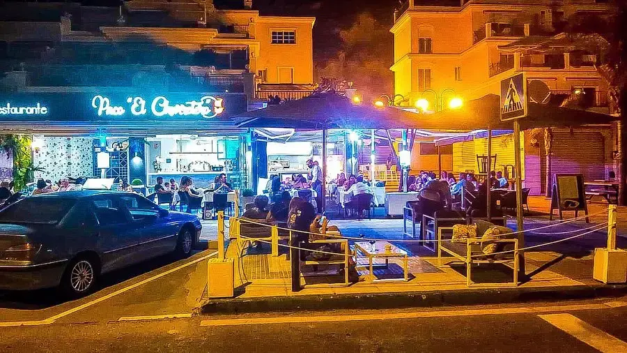 Fachada iluminada de Paco El Churretero de noche, con la terraza llena de comensales
