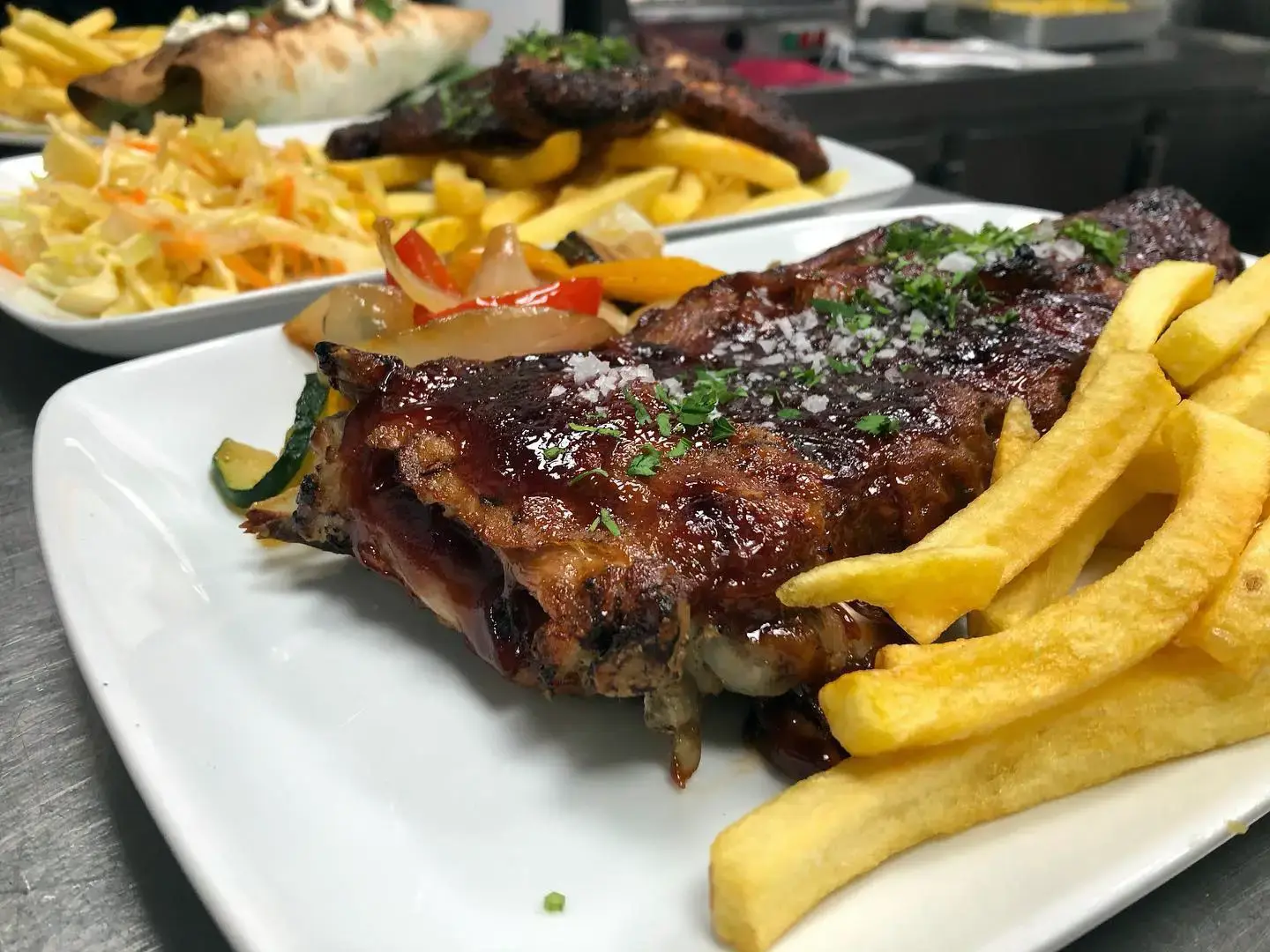 Costillas con salsa barbacoa, patatas fritas y verduras salteadas en plato blanco