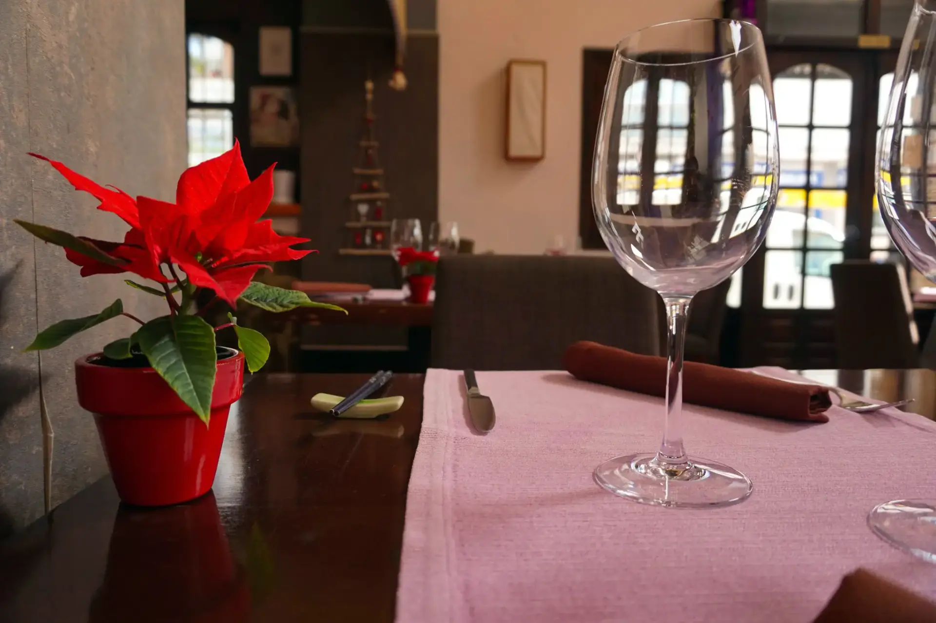 Mesa con mantel rosa, copa de vino y una flor de Pascua roja en maceta