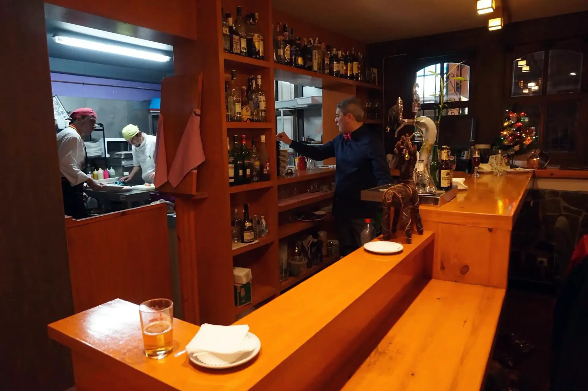Barra iluminada con botellero y la cocina abierta al fondo, con los cocineros trabajando