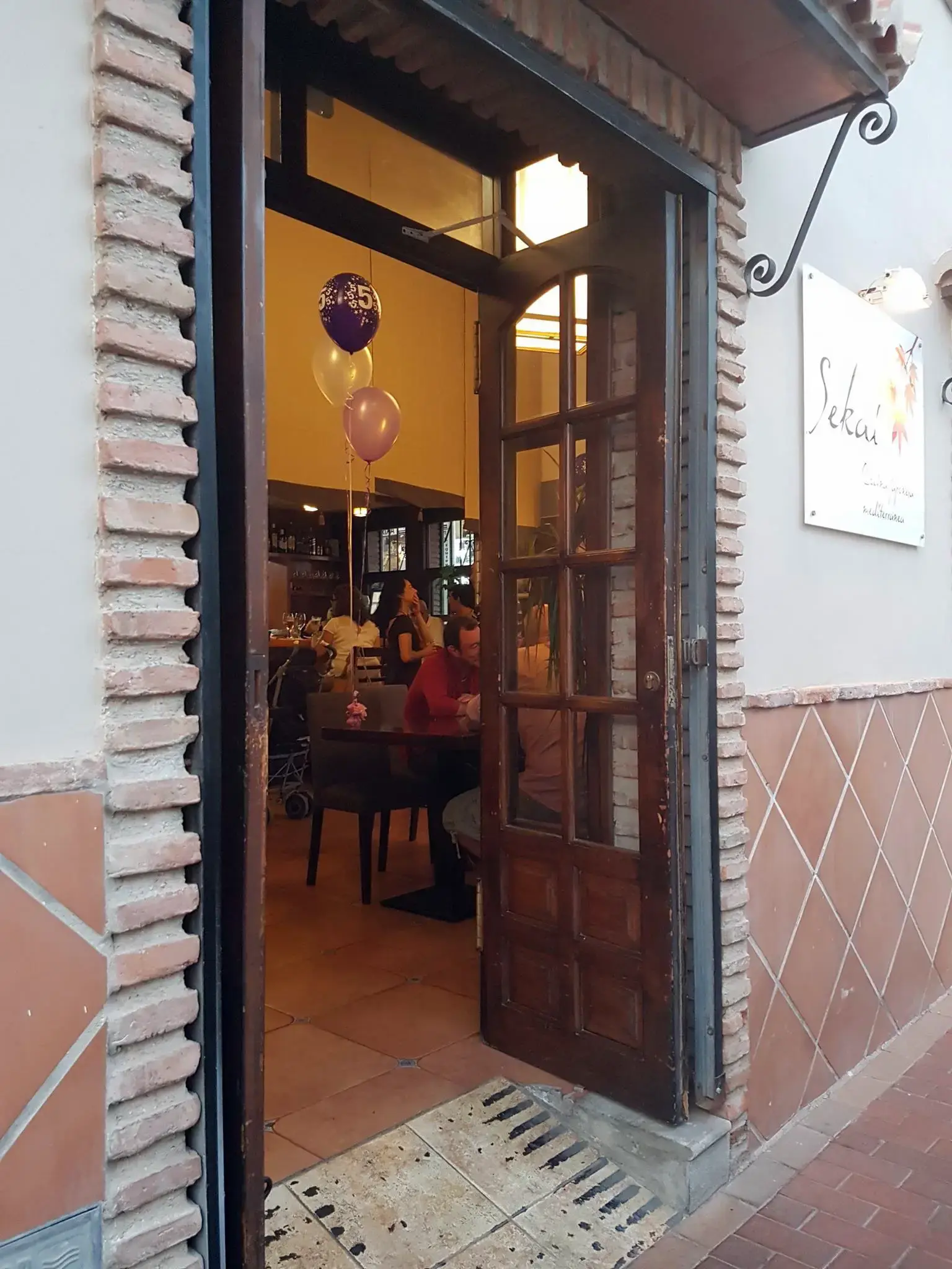 Puerta de madera abierta con el cartel de Sekai y comensales y globos en el interior