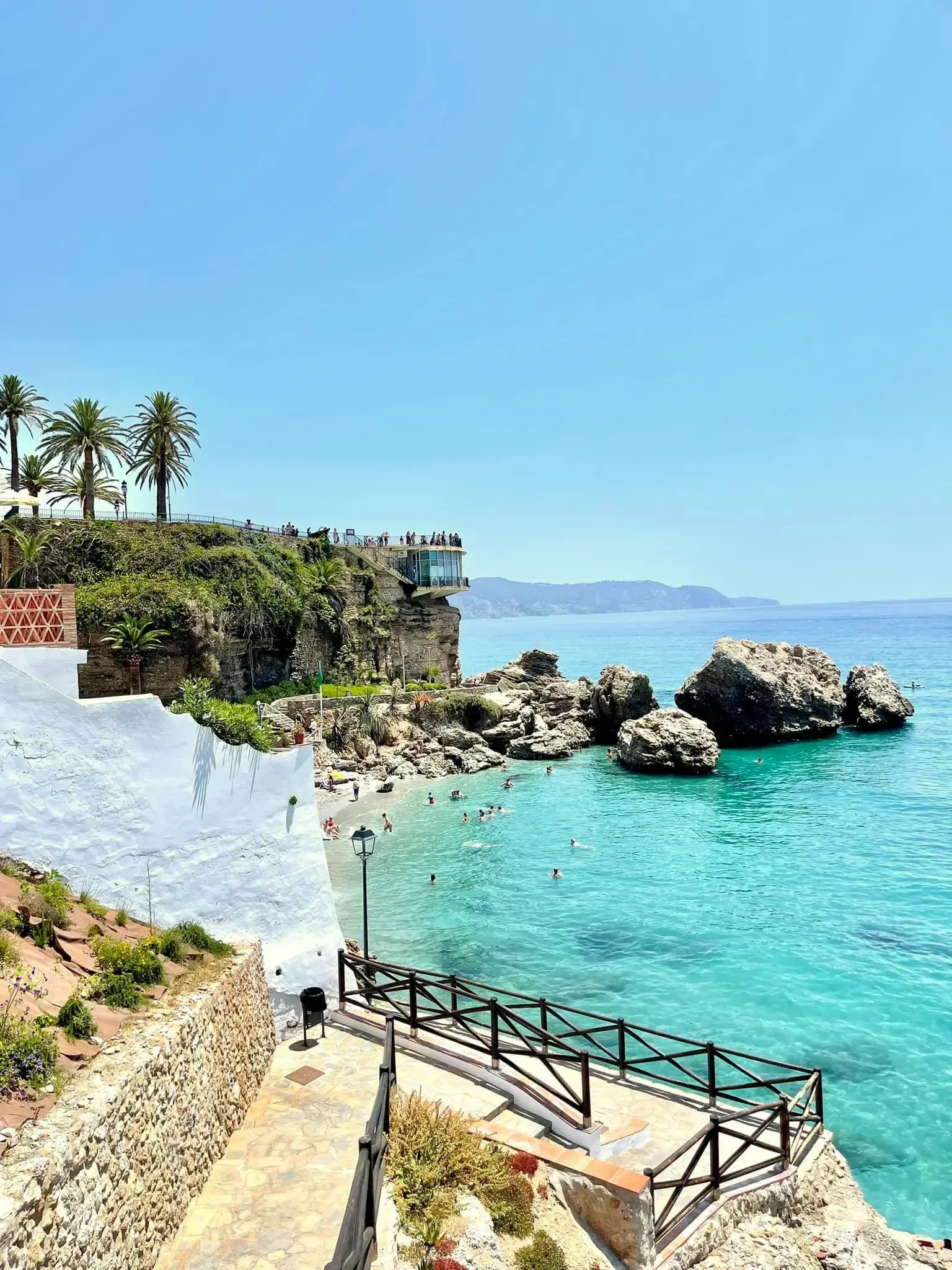 Escaleras hacia la playa Calahonda, con bañistas, rocas y el Balcón de Europa detrás
