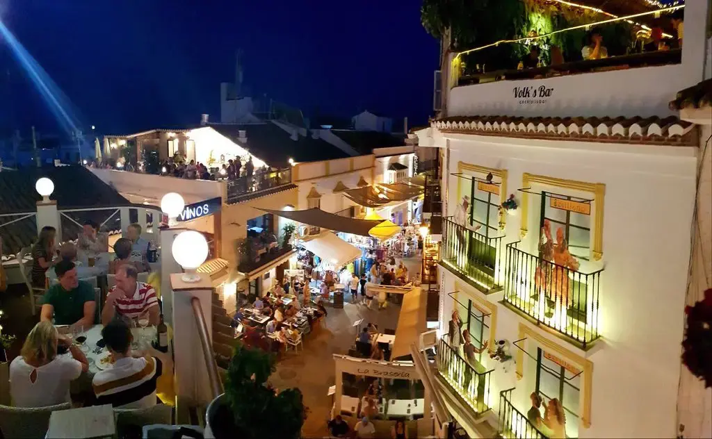 Terraza en lo alto con comensales y vista nocturna de una calle animada y llena de luces