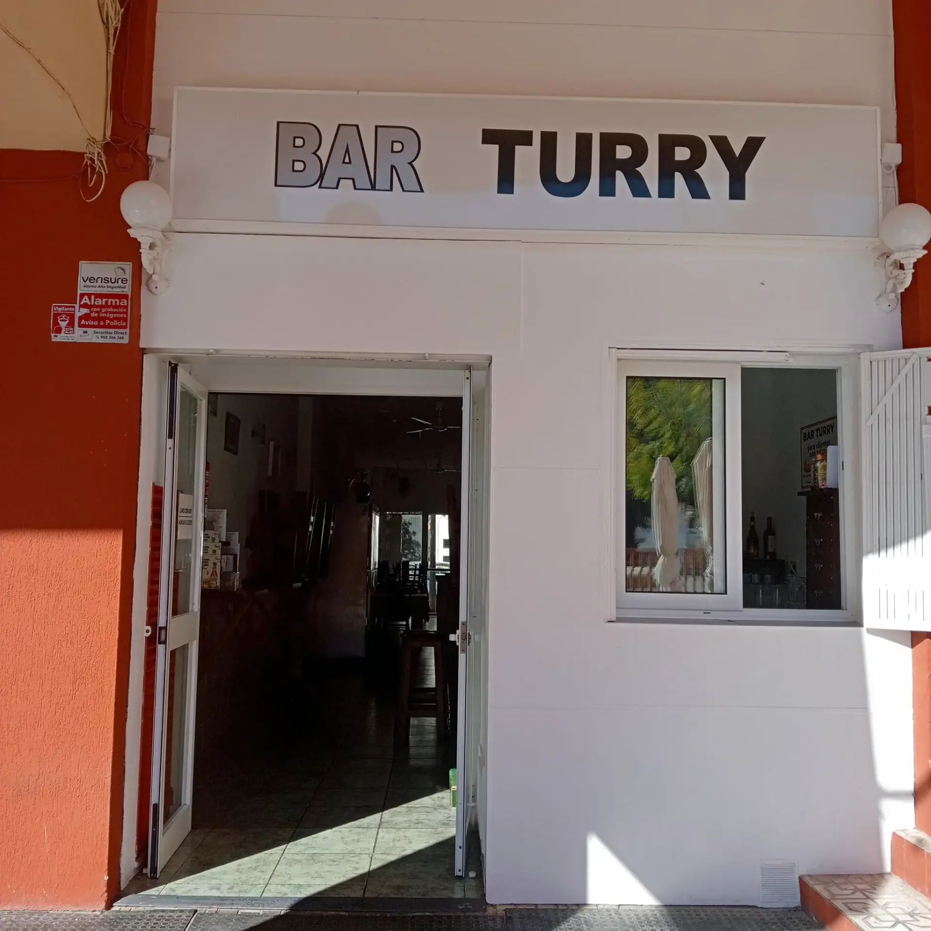 Entrada de Bar Turry con su rótulo sobre la fachada blanca y la puerta abierta