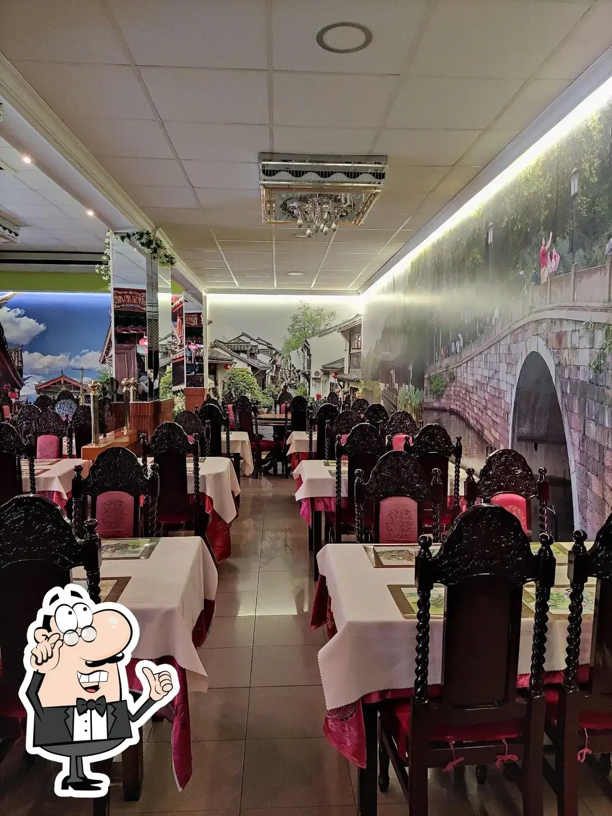 Comedor alargado con sillas talladas, manteles blancos y mural de un puente chino