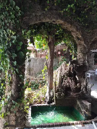 Fuente con pila de agua verde bajo un arco de piedra cubierto de hiedra
