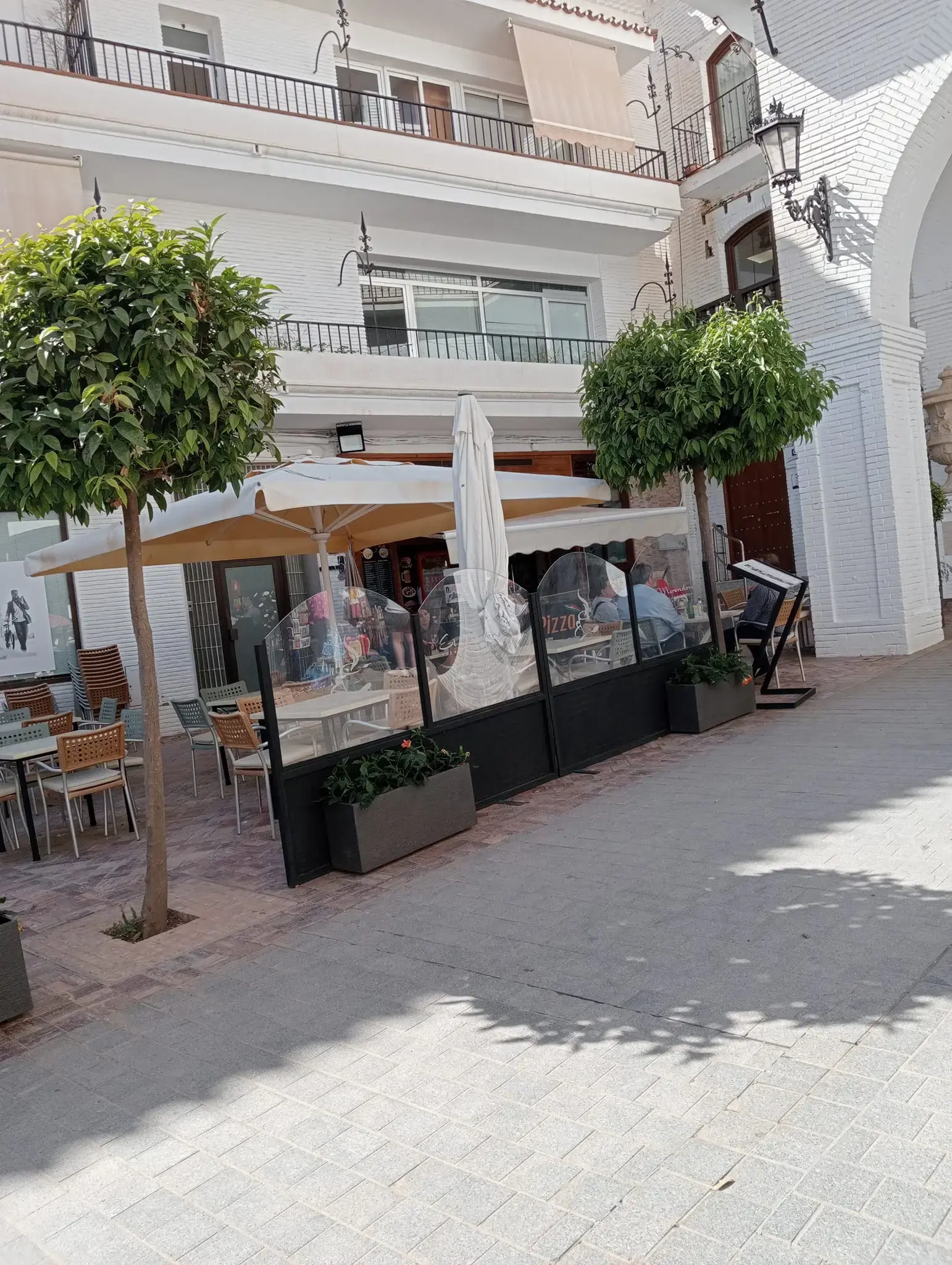 Terraza con mamparas, sombrillas y naranjos en una calle peatonal de casas blancas