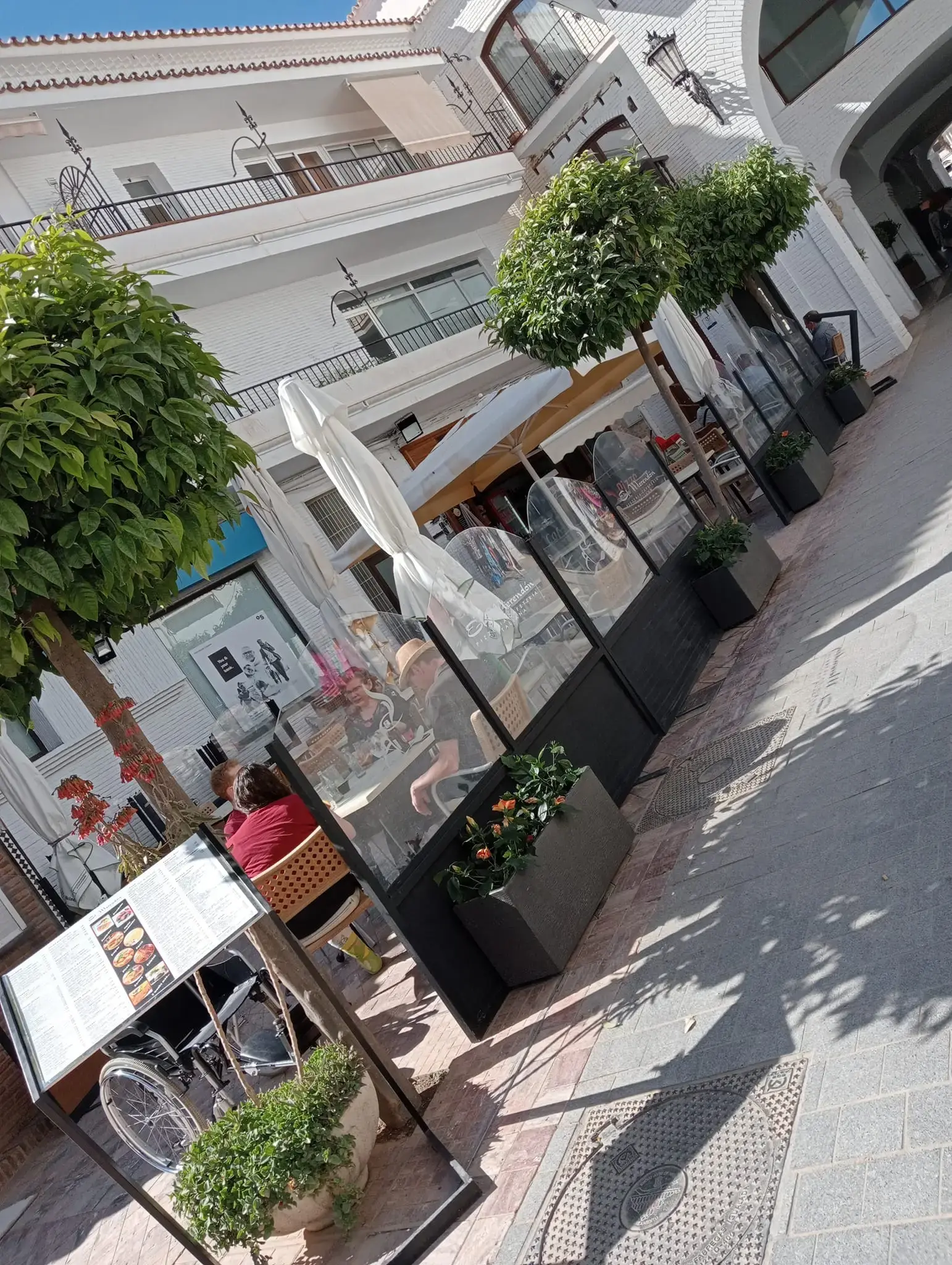 Terraza acristalada con clientes y carta expuesta en la calle, en foto inclinada
