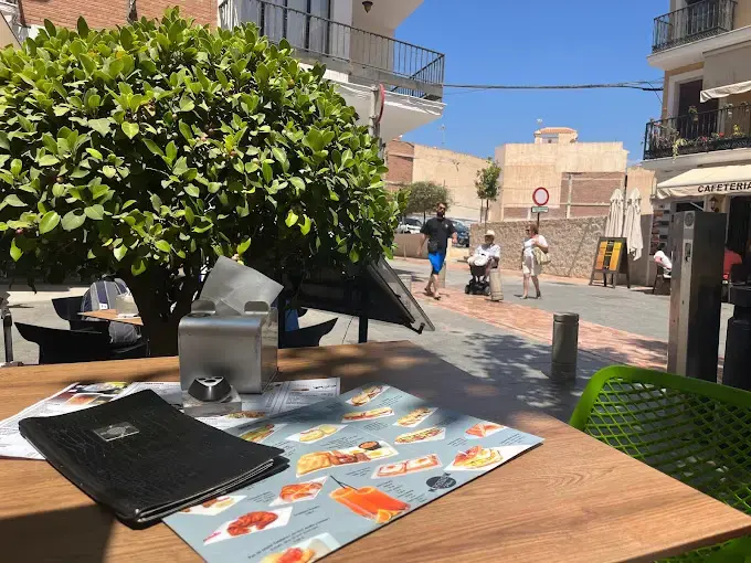 Carta con fotos de platos sobre una mesa de la terraza, con la calle soleada al fondo