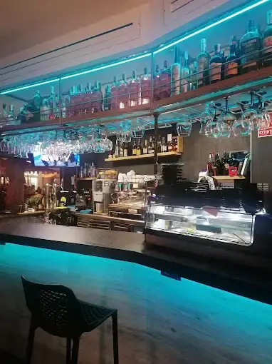 Barra interior con luces azules, botellas en estanterías y copas colgadas