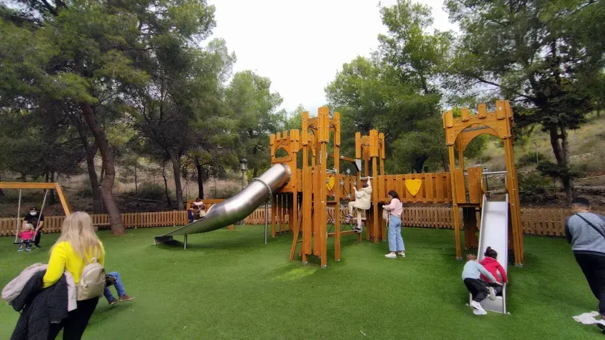 Castillo de madera con tobogán de tubo y niños jugando en el parque infantil de la Cueva de Nerja