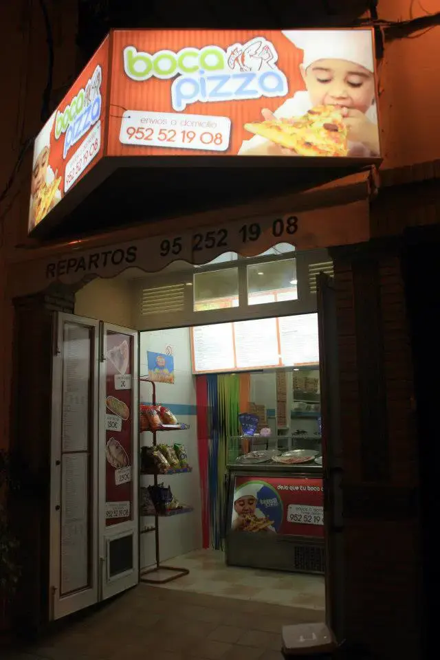 Entrada iluminada de noche con el rótulo de BocaPizza y el mostrador al fondo