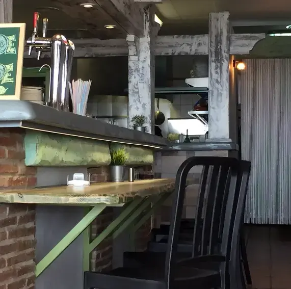 Barra de ladrillo y madera verde con grifo de cerveza y taburetes negros