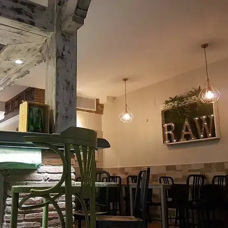 Interior de noche con lámparas geométricas y el rótulo luminoso RAW en la pared