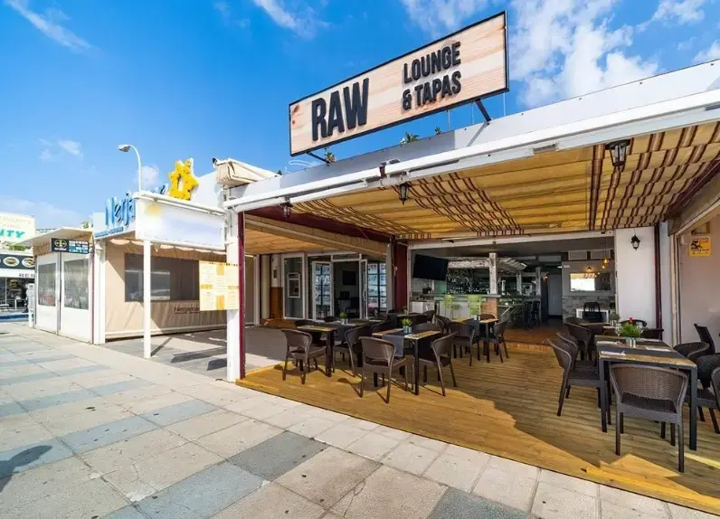 Fachada de RAW Lounge & Tapas desde la acera, con la terraza abierta bajo el cielo azul