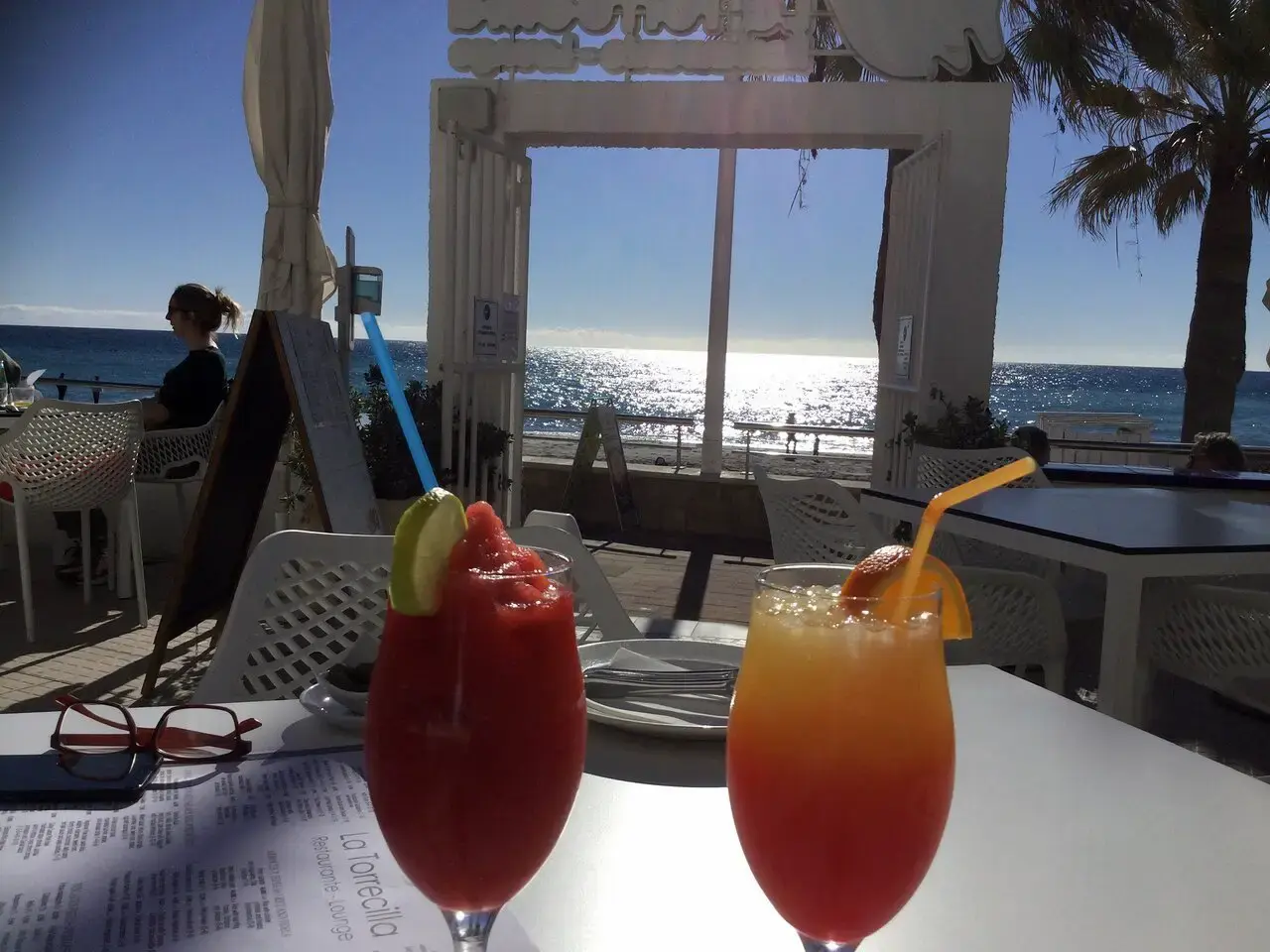 Dos cócteles de colores en una mesa de la terraza con el mar brillando al fondo