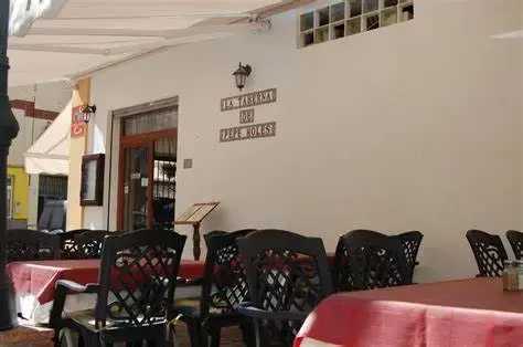 Terraza con manteles rojos y sillas de forja junto al rótulo de azulejos de la taberna