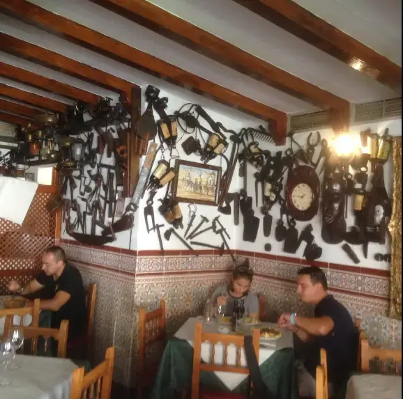 Comedor con zócalo de azulejos y paredes llenas de aperos antiguos y faroles
