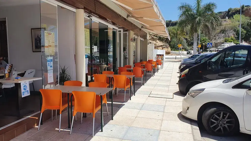 Terraza de sillas naranjas en la acera soleada, bajo un toldo y junto a la calle