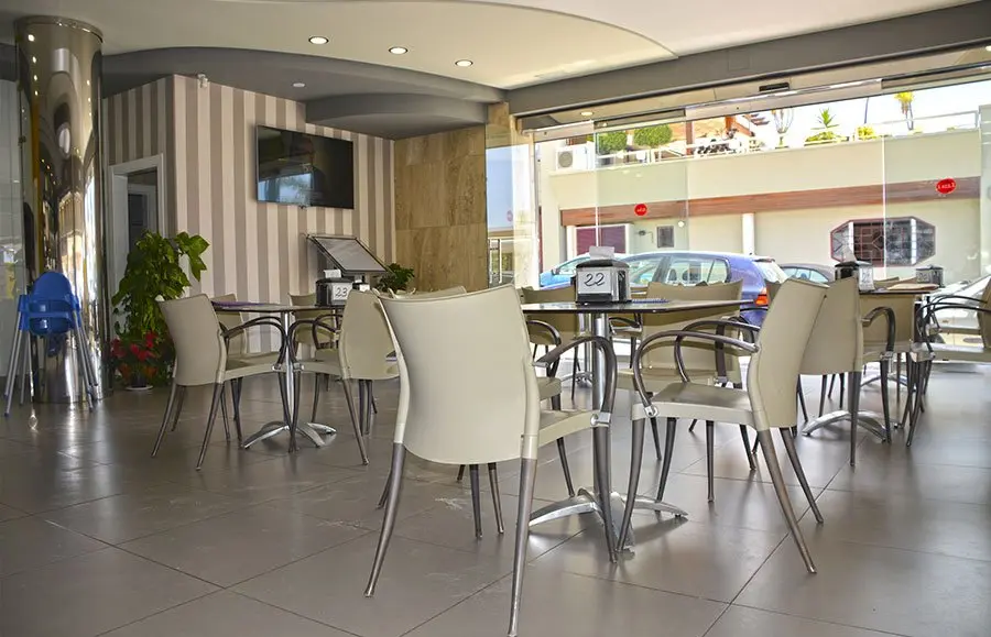 Salón interior con sillas blancas, mesas altas y grandes ventanales a la calle