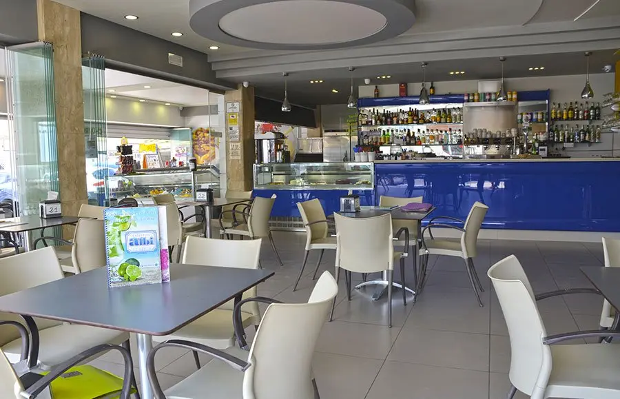 Comedor con mesas grises y la barra azul con botellero al fondo
