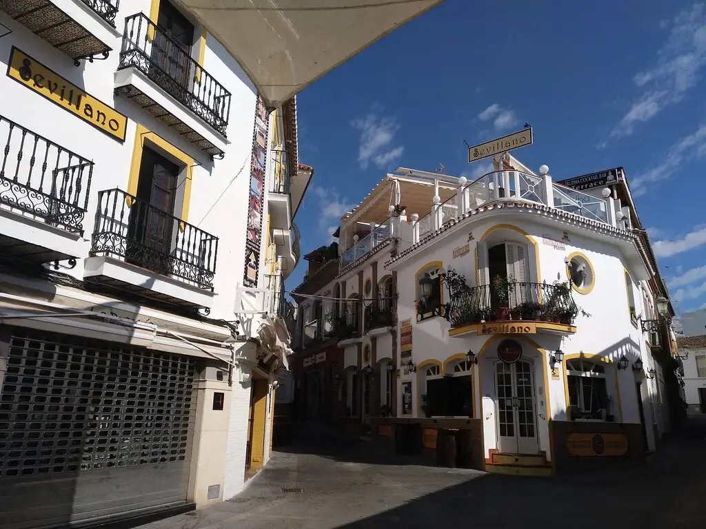 Edificio blanco de esquina de El Sevillano con balcones de forja en una calle del centro