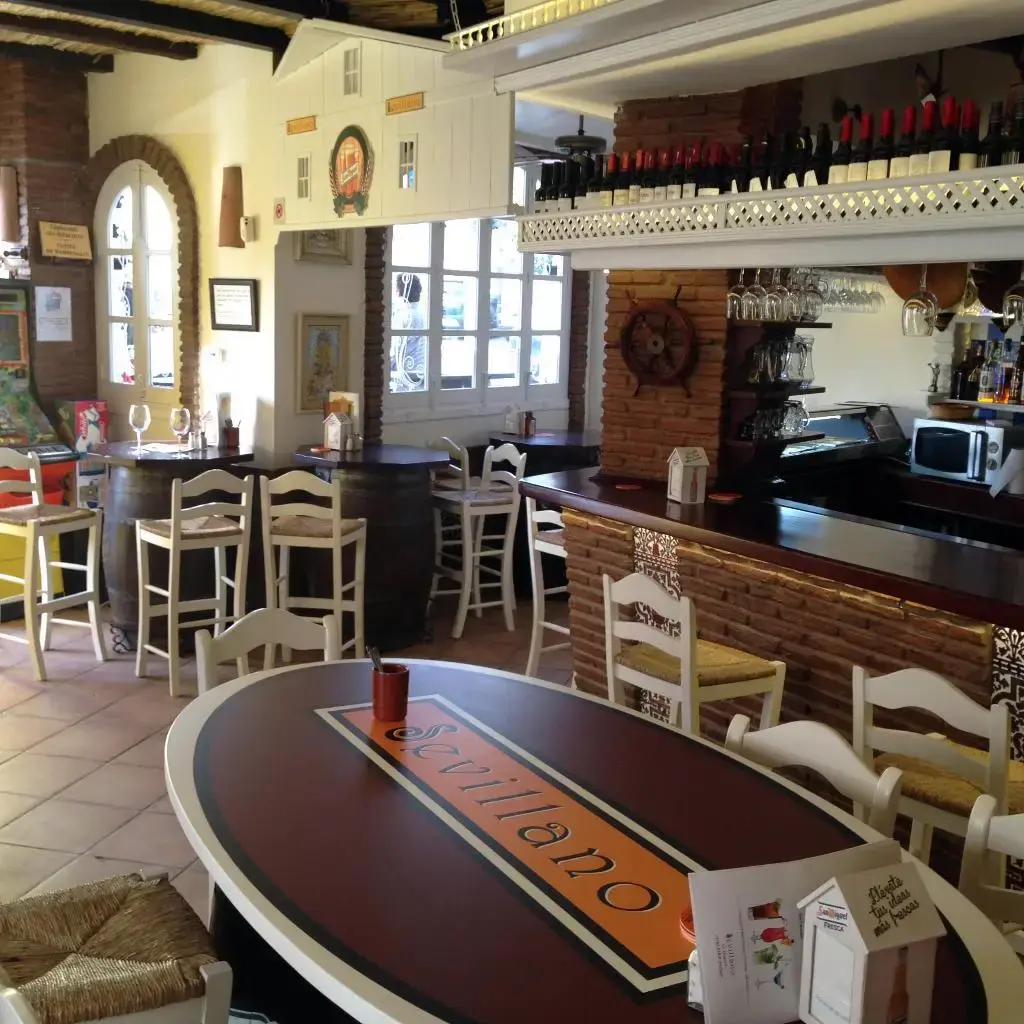Interior de El Sevillano con mesa de barril, barra de ladrillo y botellas de vino en lo alto