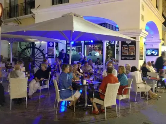 Terraza de Kronox Café de noche, llena de clientes bajo sombrillas e iluminación azul