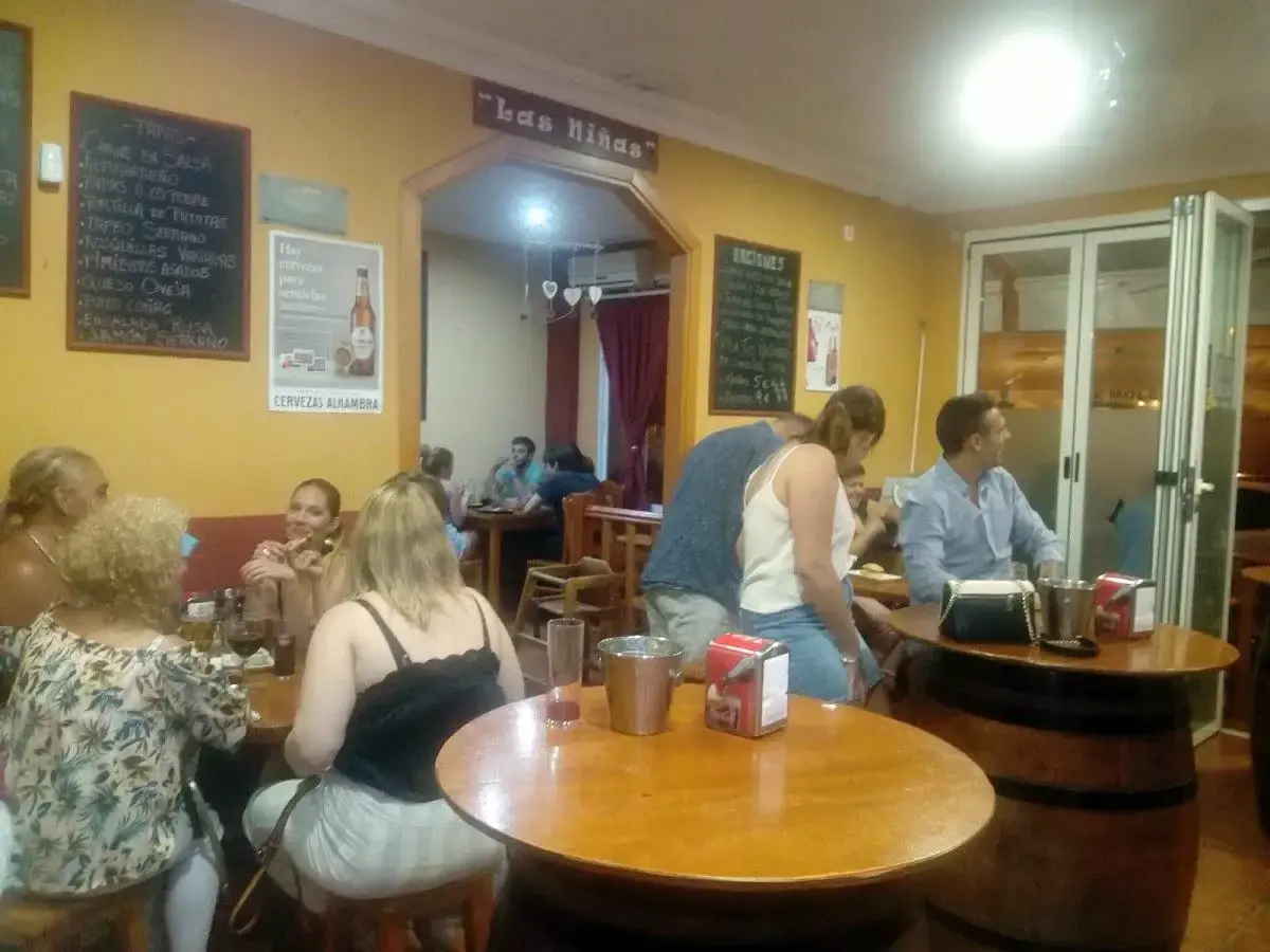 Clientes en mesas de toneles y pizarras con tapas en el interior del bar por la noche