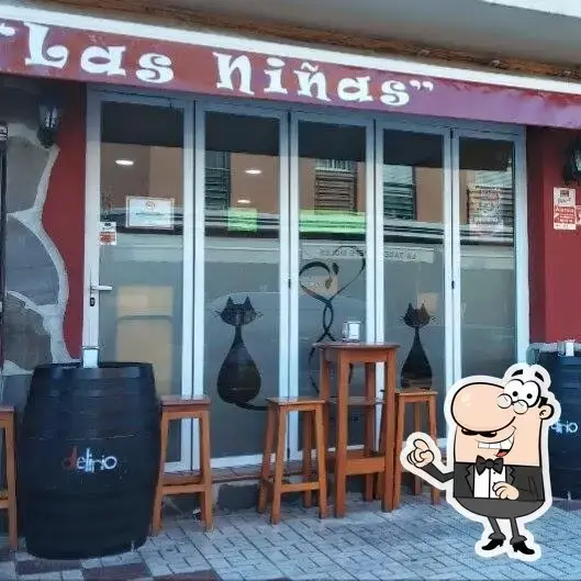 Fachada de Bar Las Niñas de Motril con toneles, taburetes altos y gatos en el cristal