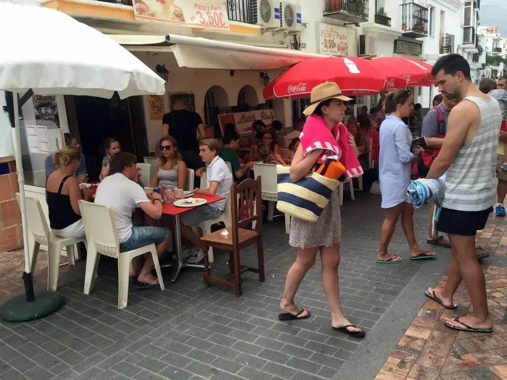 Clientes comiendo en la terraza y paseantes con bolsas de playa por la calle