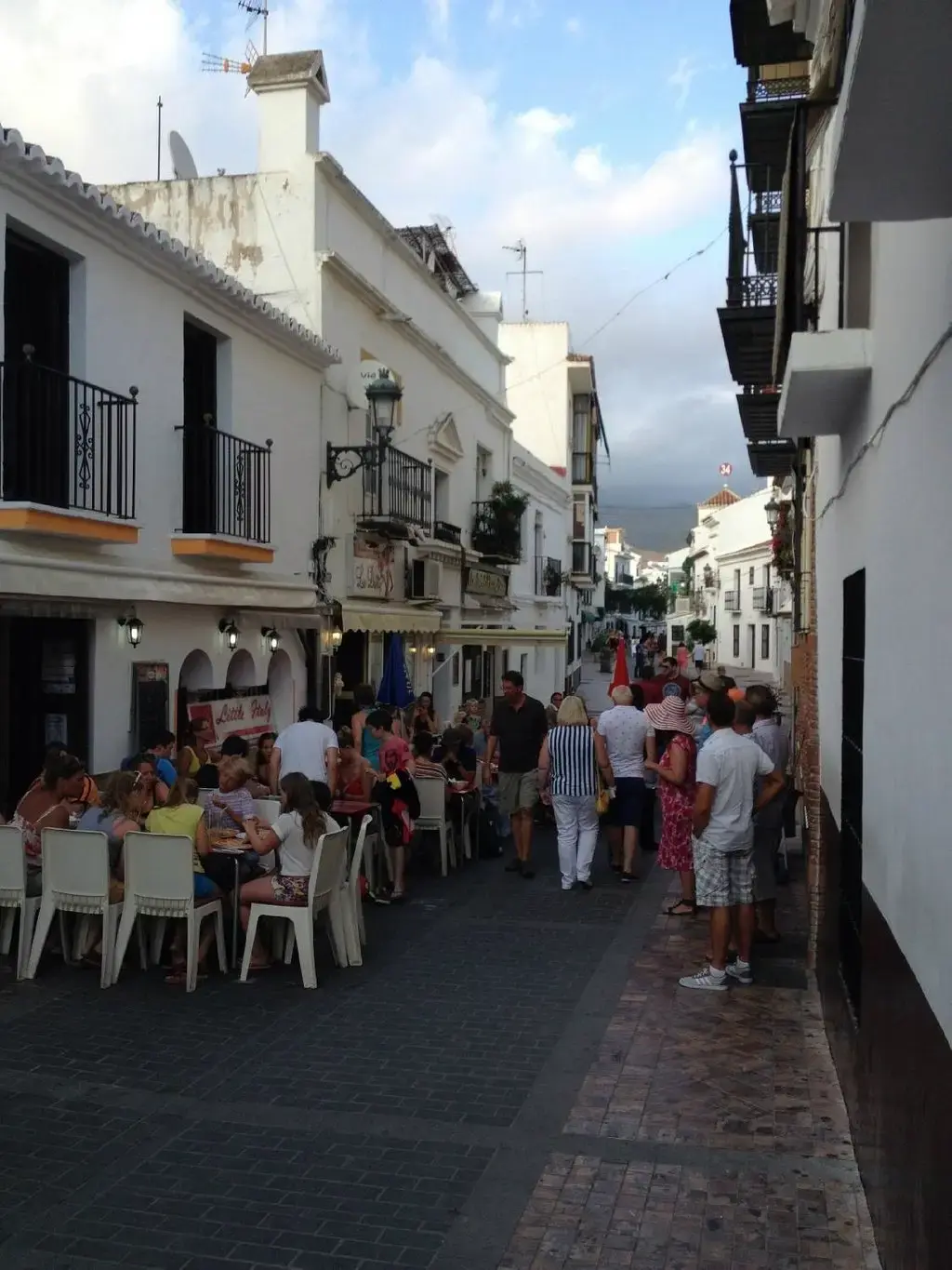 Calle encalada con la terraza llena de comensales y gente paseando al caer la tarde