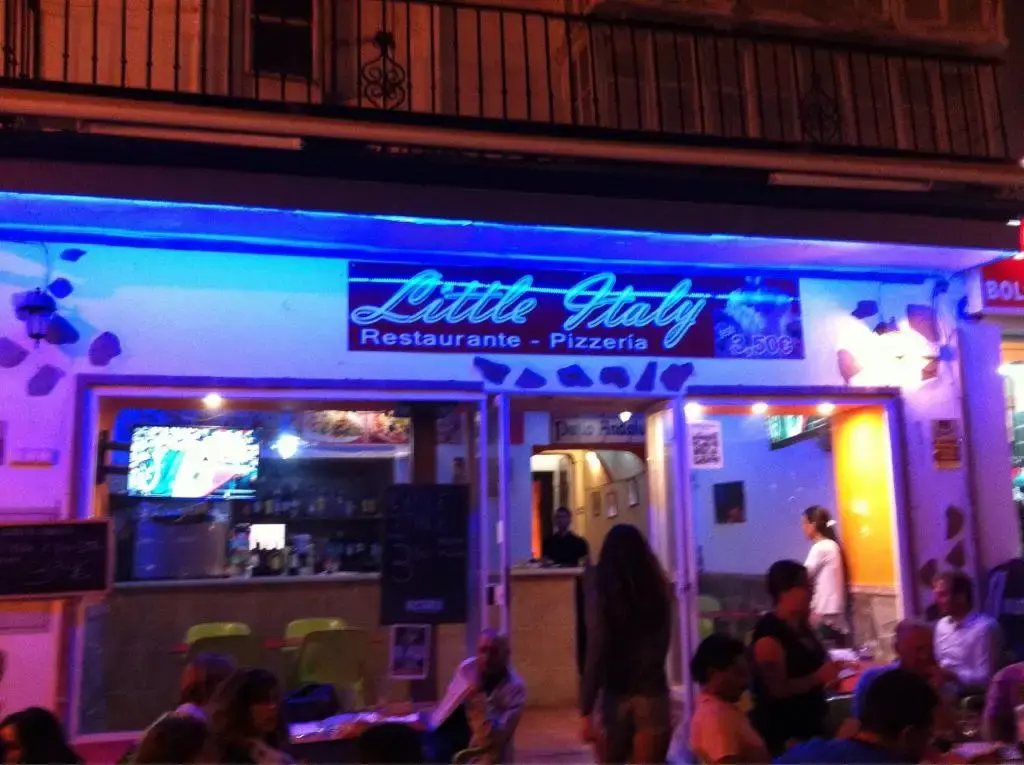 Fachada de Little Italy Restaurante Pizzería de noche, con rótulo y luces azules
