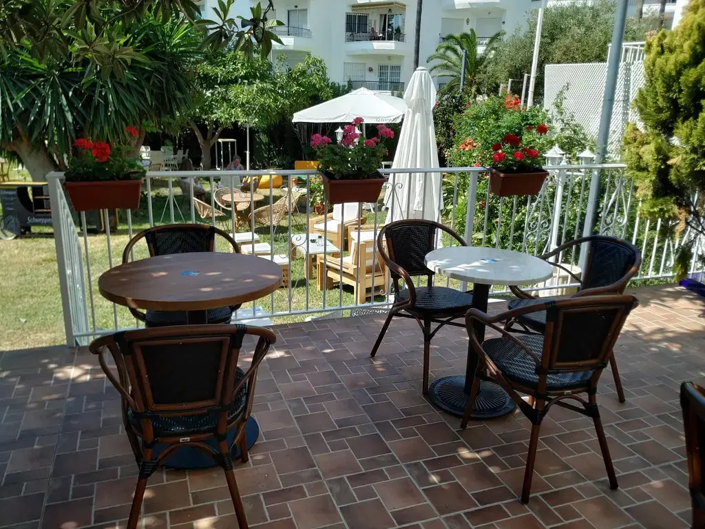 Mesas y sillas de terraza junto a la barandilla con macetas de flores y el jardín detrás