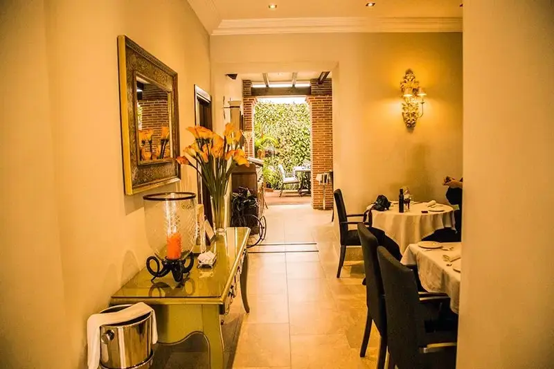 Pasillo con espejo dorado y calas naranjas que lleva al patio ajardinado