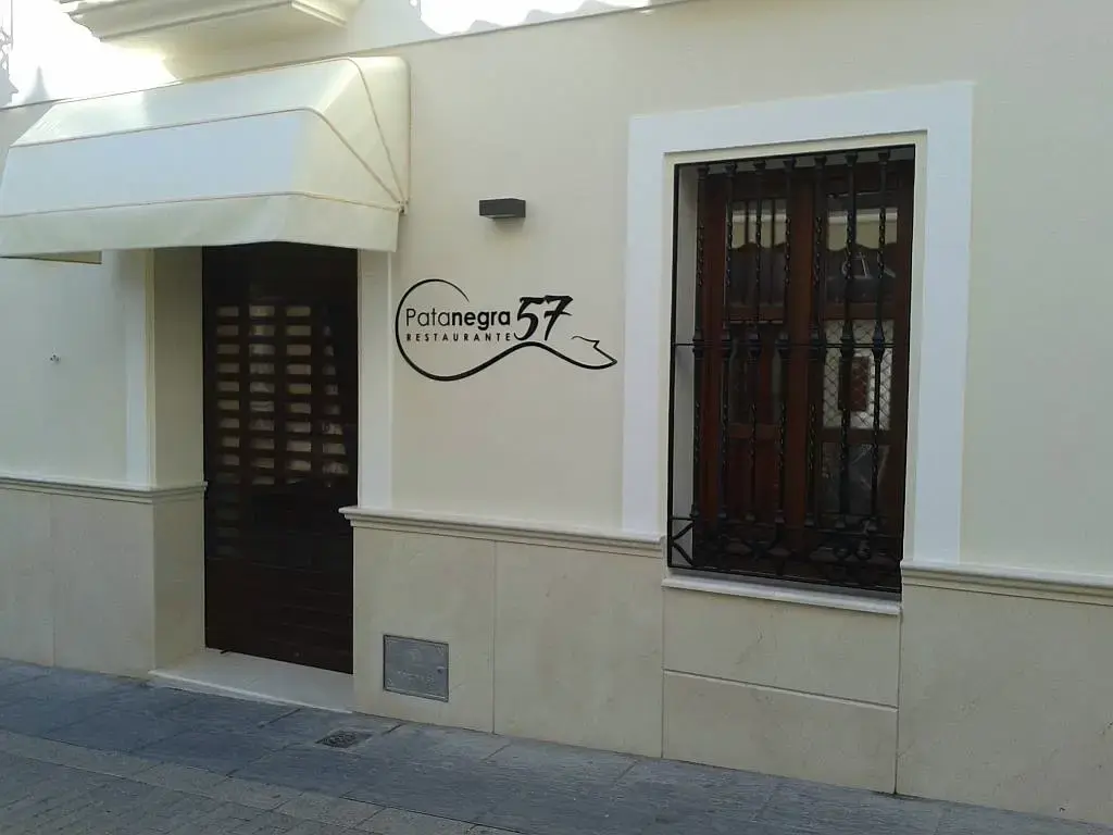 Entrada del Restaurante Pata Negra 57 con su logotipo en la fachada crema