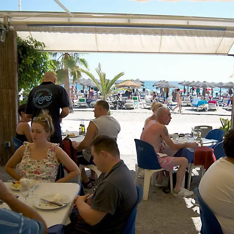 Clientes comiendo en la terraza con hamacas y sombrillas de la playa al fondo