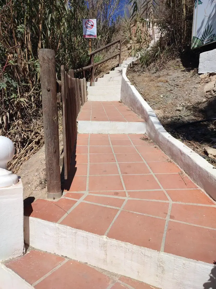 Escalera de baldosas con barandilla de madera en el acceso a la playa Piedra de Tarzán
