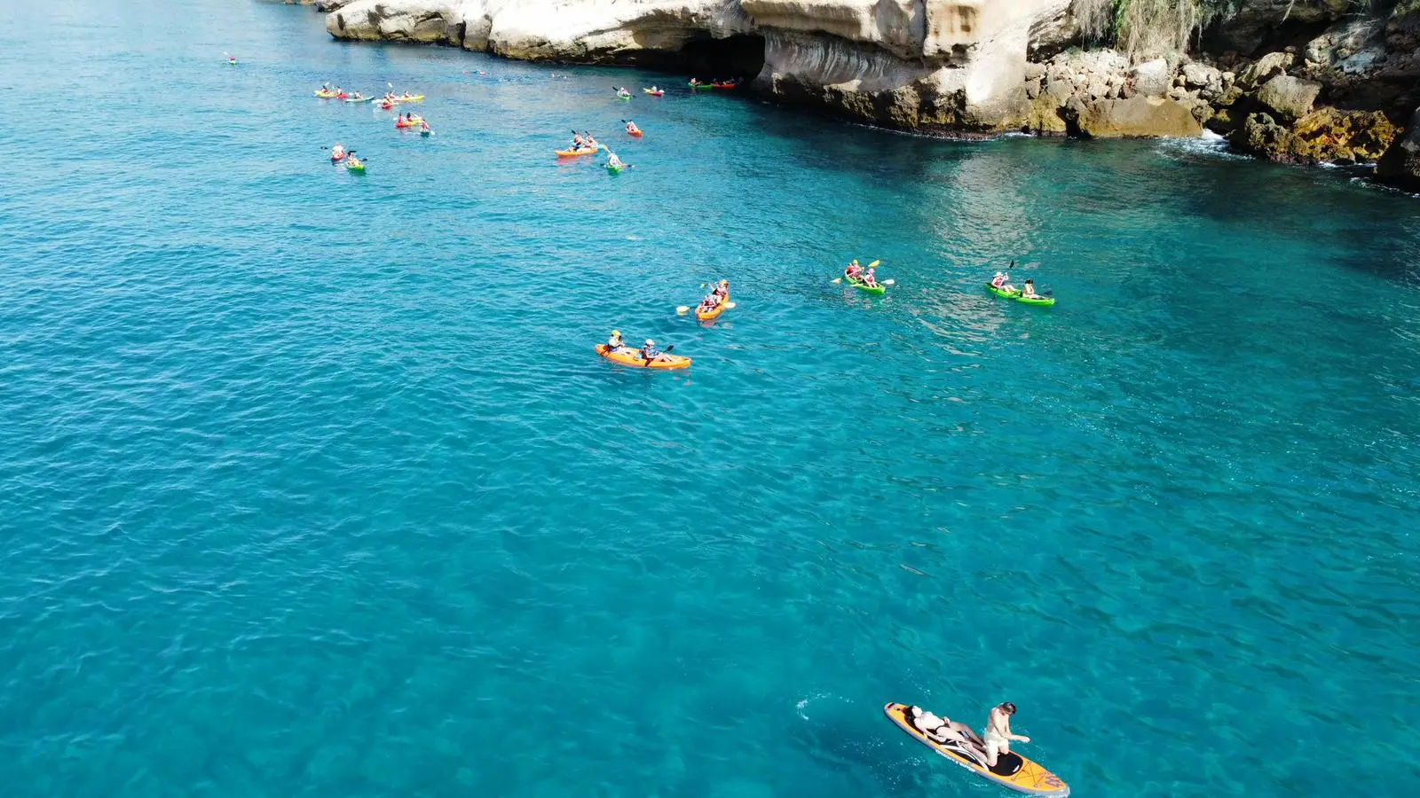 Grupo de kayaks y una tabla de paddle surf en aguas turquesa bajo los acantilados