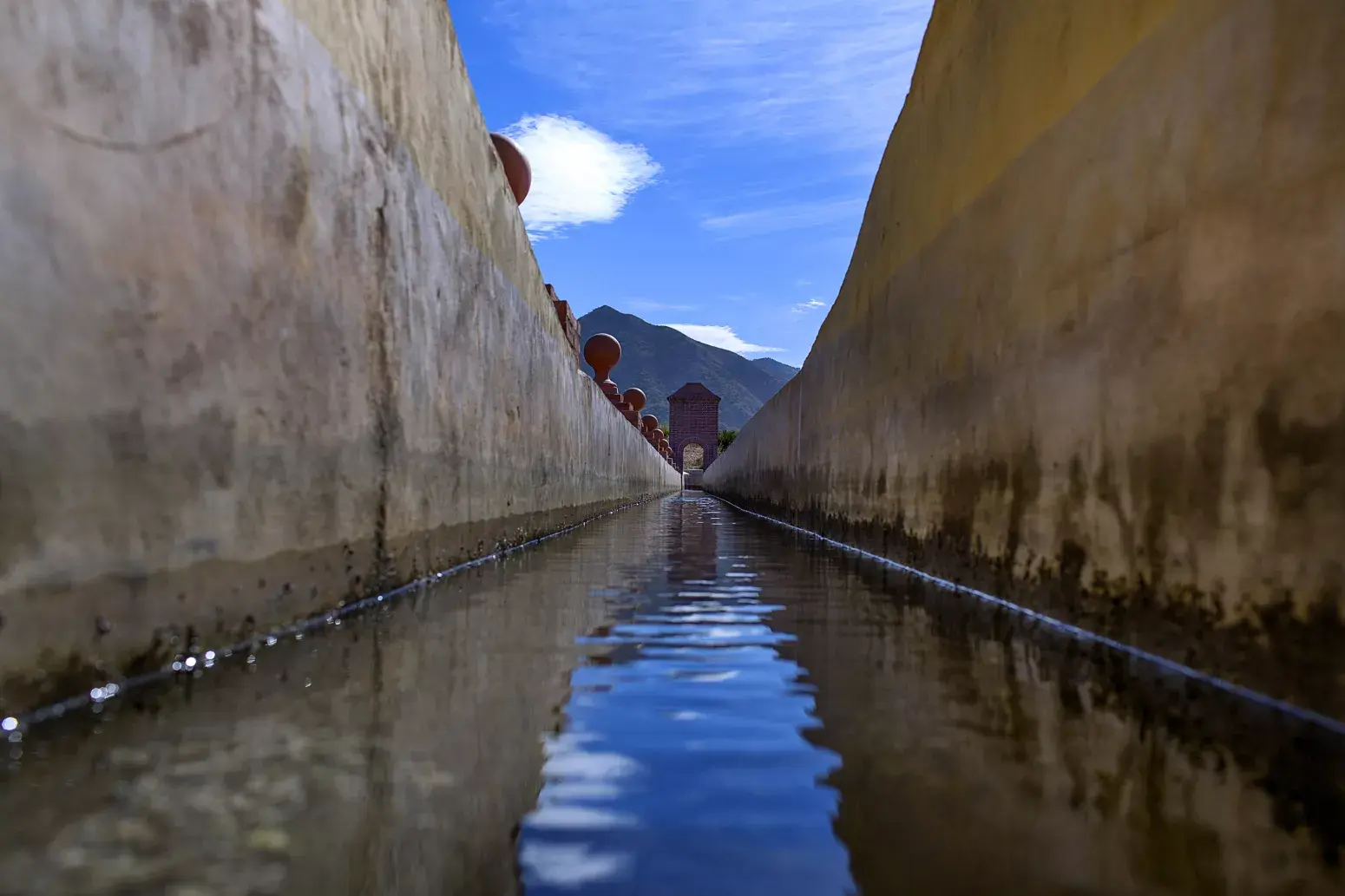 Agua corriendo por el canal del acueducto entre muros encalados, bajo un cielo azul
