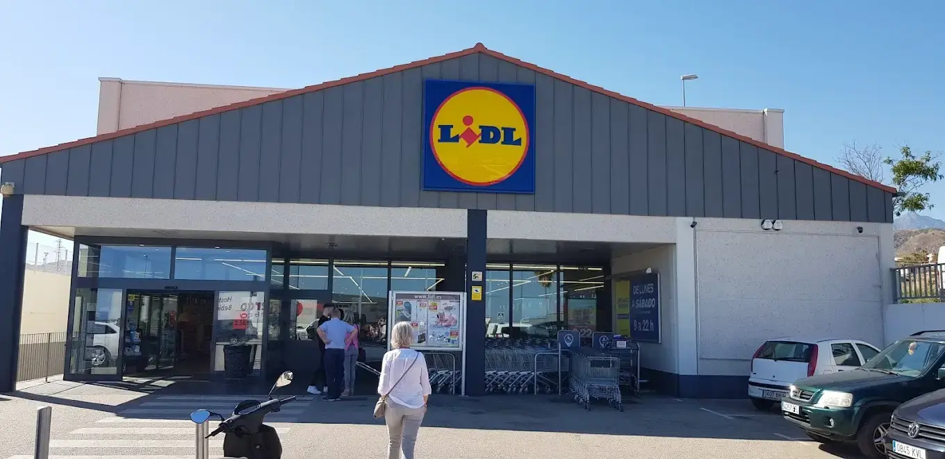 Entrada de un supermercado Lidl con tejado a dos aguas, carros y clientes en la puerta
