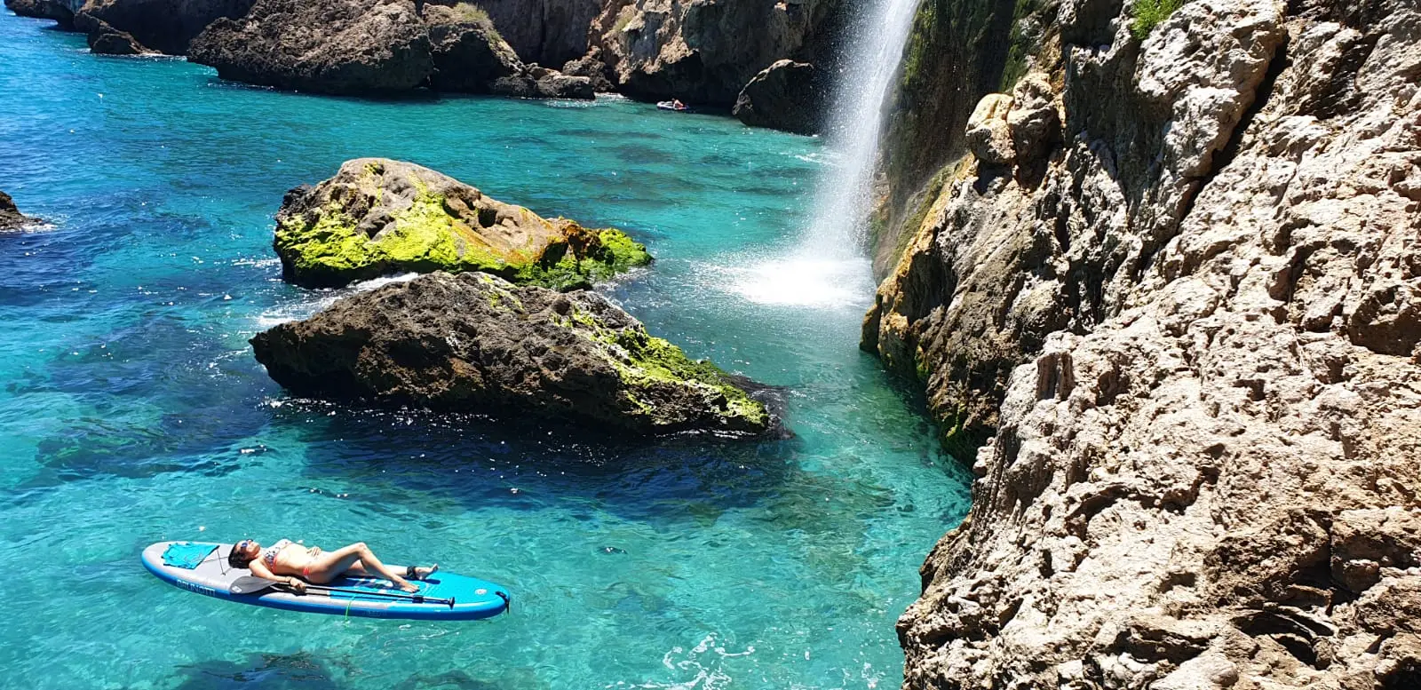 Bañista tumbada al sol sobre una tabla de paddle surf junto a la cascada de Maro