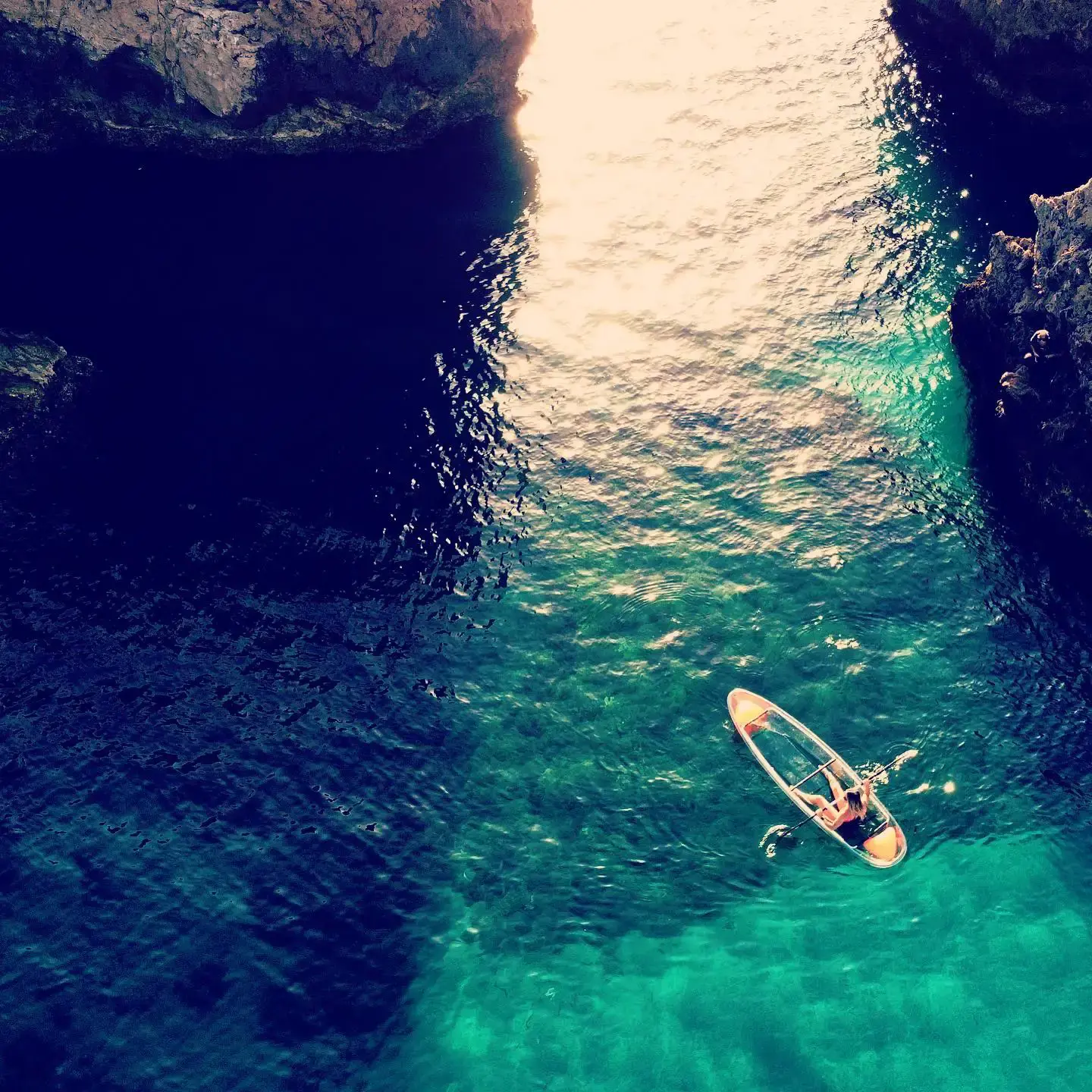 Kayak transparente entre dos paredes de roca, visto desde arriba con el sol reflejado en el agua