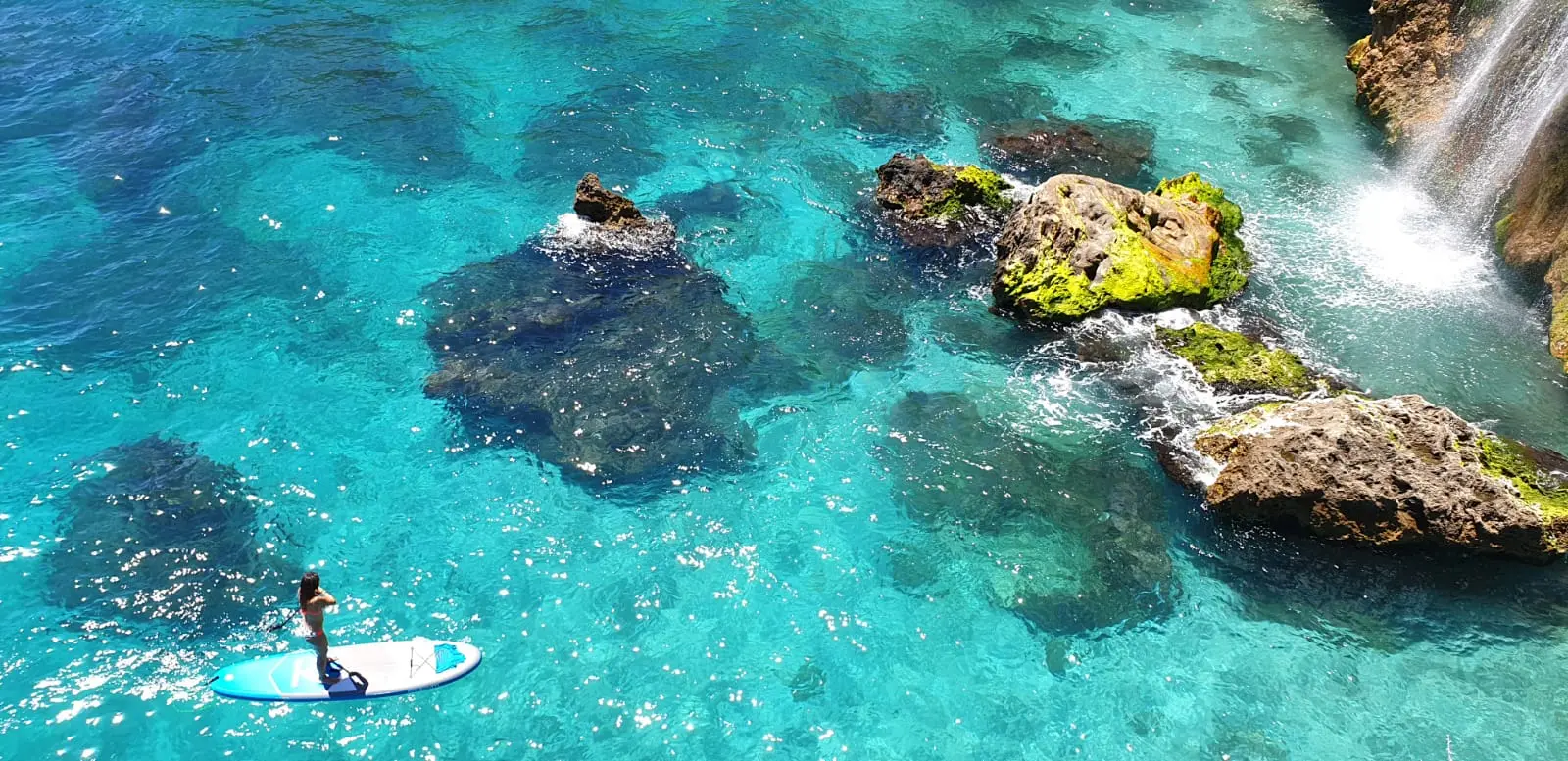 Tabla de paddle surf sobre aguas cristalinas y rocas sumergidas cerca de una cascada